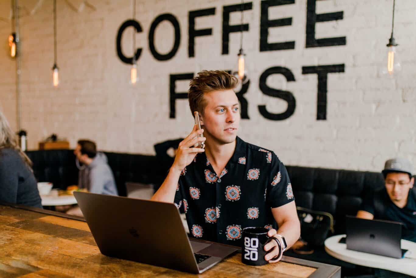 Mann am Telefon und mit einem Computer in einer Kaffeebar